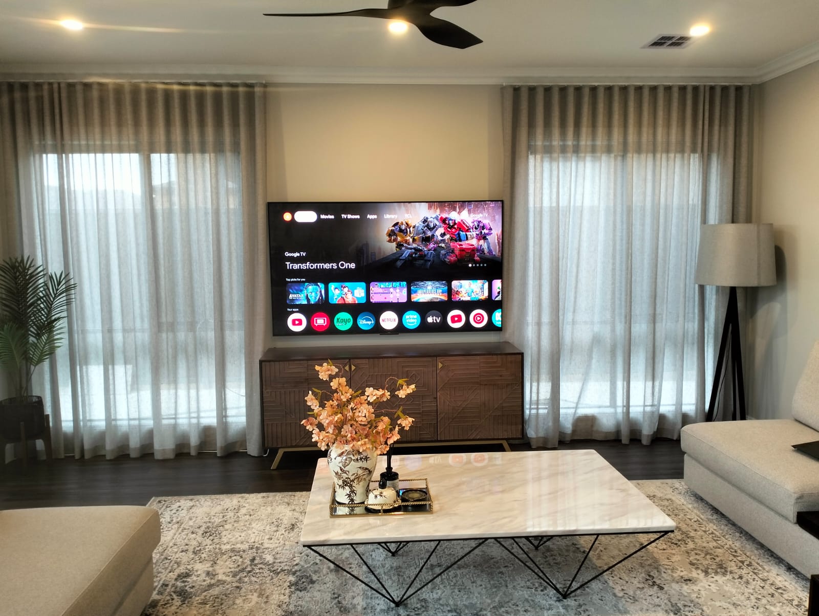 Modern living room with a wall-mounted TV displaying a streaming interface, a marble coffee table, and a stylish entertainment unit.